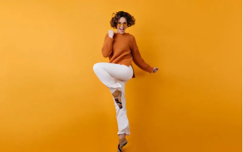Short bob haircut in the form of a mushroom on a woman in an orange sweater and white pants