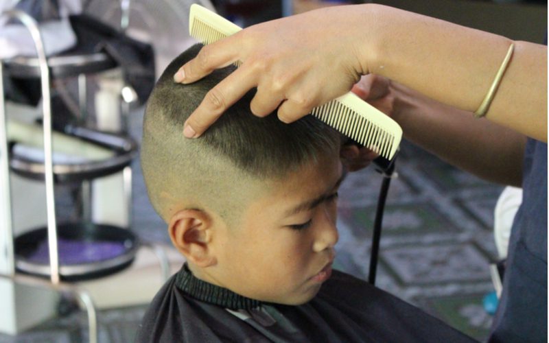 Younger guy getting a buzzcut from a barber holding a comb in his left hand