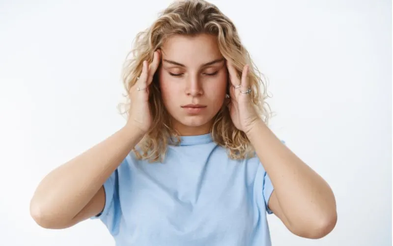 Lady in a blue shirt holding her head because she has a migraine