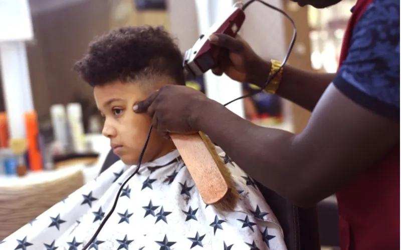 Kid getting an afro buzz from a barber holding a long brush to his chin