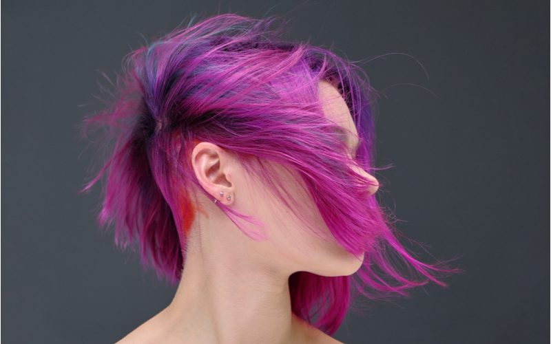 Woman with a light purple feathered undercut haircut looks to her left and lets her hair slap her face