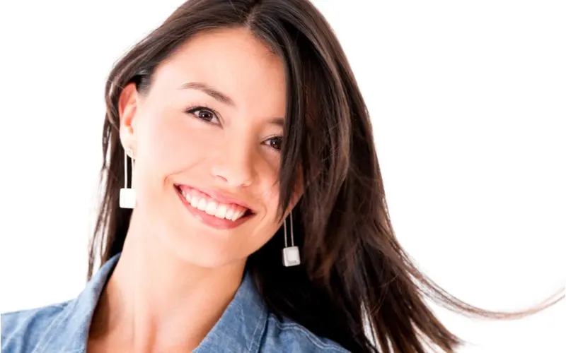 Gal in a jean jacket with choppy long feathered hair smiles and wears square metal earrings