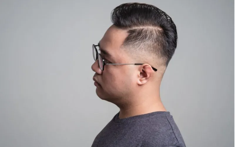 Man with a Comb-Over Low Fade haircut in a side profile image with a hard part on the left part of his head