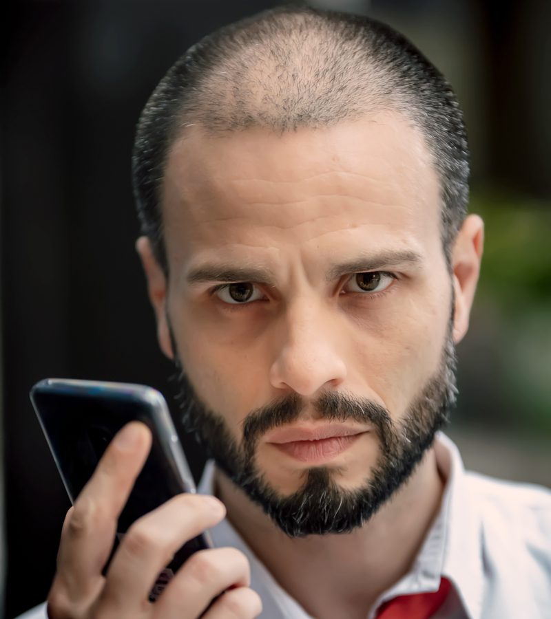 Balding man with a longer buzzcut holds a phone to his face