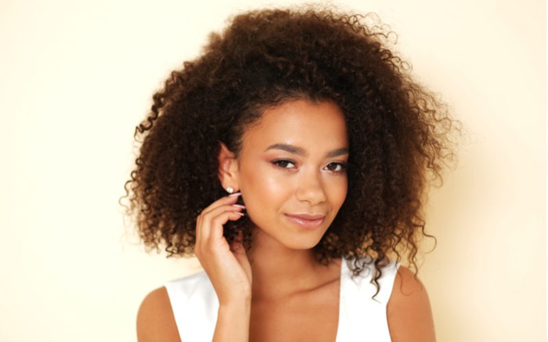 Gal with puffy natural hair grins while looking ahead and holding her ear