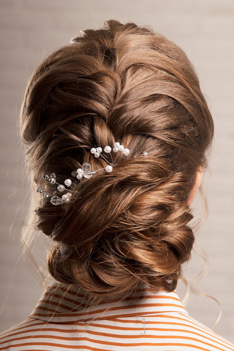 Mother of the groom hairstyle of a low bun with floral barrettes looks away from the reader but still looks elegant 