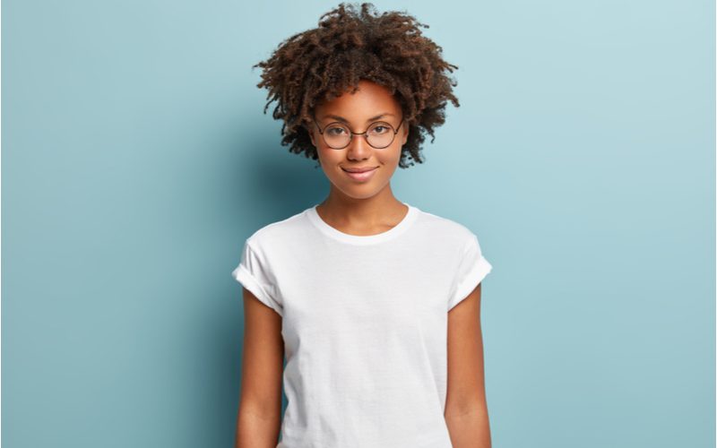 Lady with high definition coils stands in a white shirt in a blue room grinning at the reader