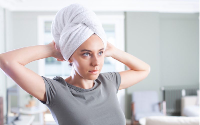 Image of a woman showing us how to wrap hair with a towel wearing a grey crew neck shirt