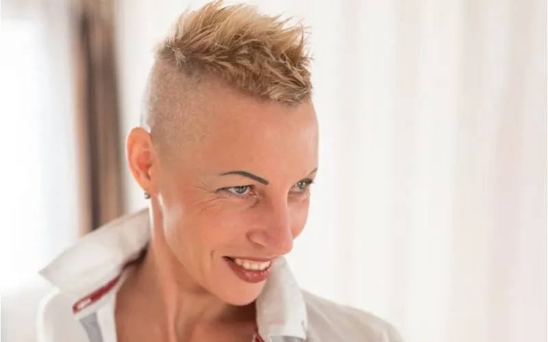 Lesbian gal with a feathered haircut on top with shaved sides grins while wearing a white collared shirt with a popped collar