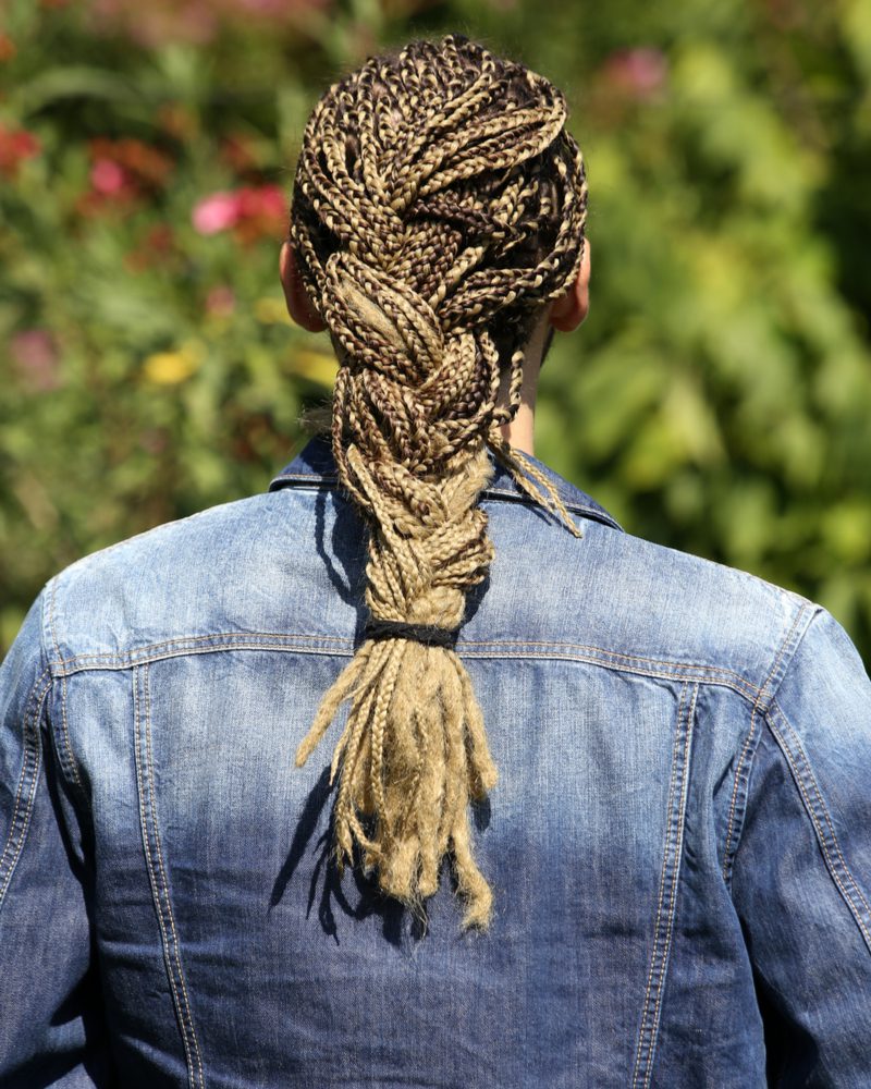 Braided Box braids for men on a guy in a jean jacket looking toward a bunch of trees