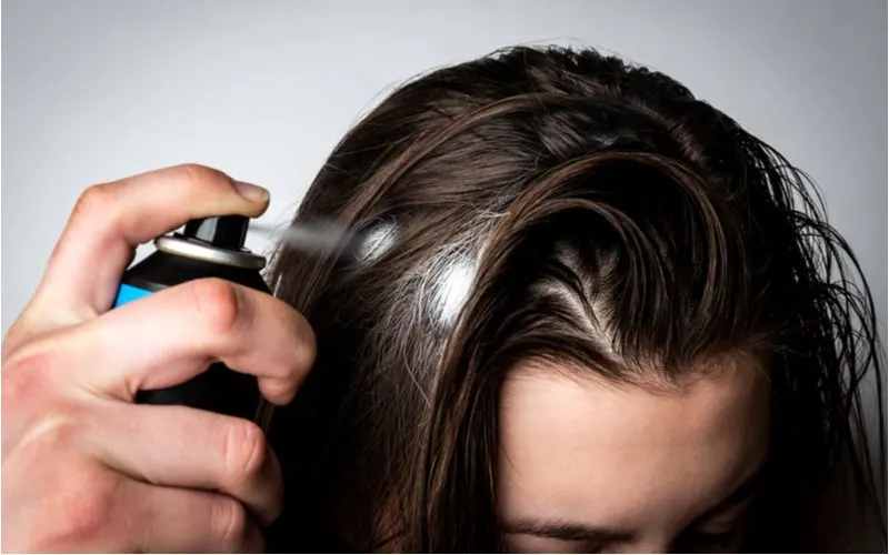 To help get rid of greasy hair, a woman using dry shampoo to absorb the excess moisture