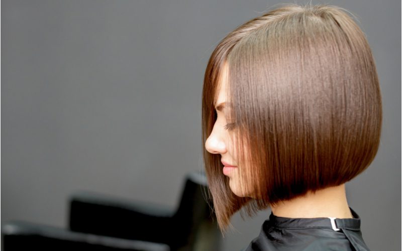 Side profile of a woman with a short bob haircut in a cape looking straight ahead from a salon chair