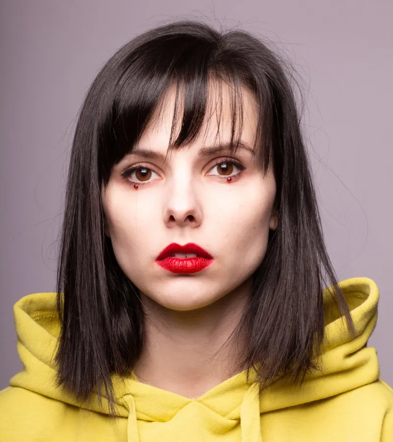 Choppy long bob with whispy bangs on a woman in a yellow hooded sweatshirt