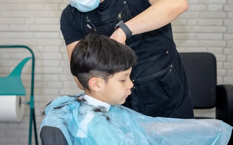 Kid getting a bowl cut buzzcut or undercut style from a hairdresser in a mask