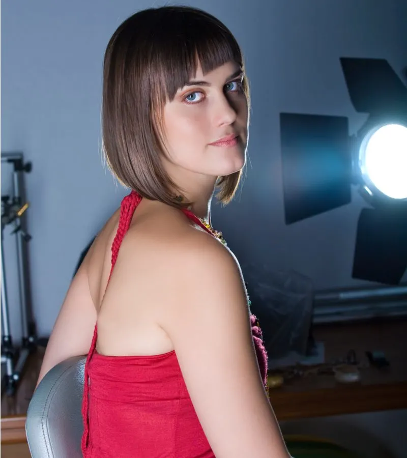 A-Line Inverted Lob With Asymmetrical Bangs on a woman in a red dress in front of a studio light
