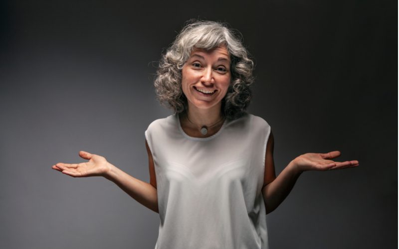 Woman holding her arms up in a questioning post for a piece on what causes grey hair