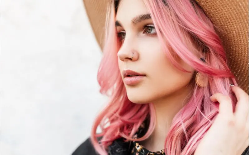 Woman with pink hair wears a boho hat for a piece on how to cut curtain bangs