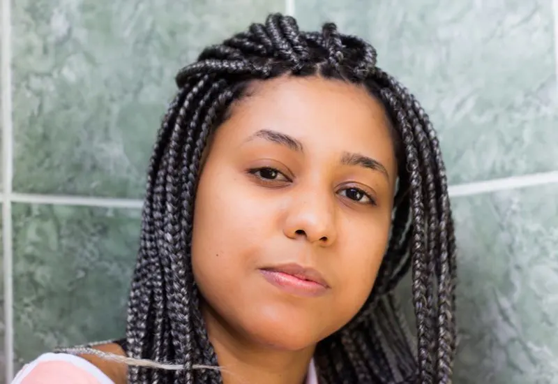 Pushed-Back Braids With Silver Highlights on a black woman in front of a slate wall