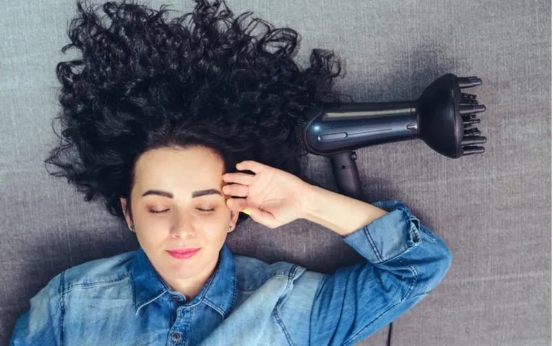 Happy woman lying on a floor with a hair diffuser next to her head holding her forehead with her left hand