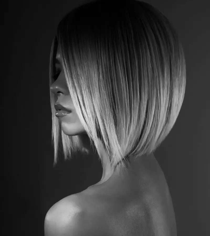 Woman with a blonde midi inverted bob haircut stands in a dark room for a black and white image