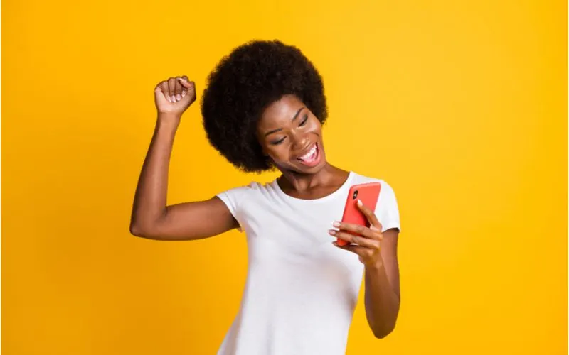 Gal with a traditional '70s afro holding a phone and cheering with her hand above her head