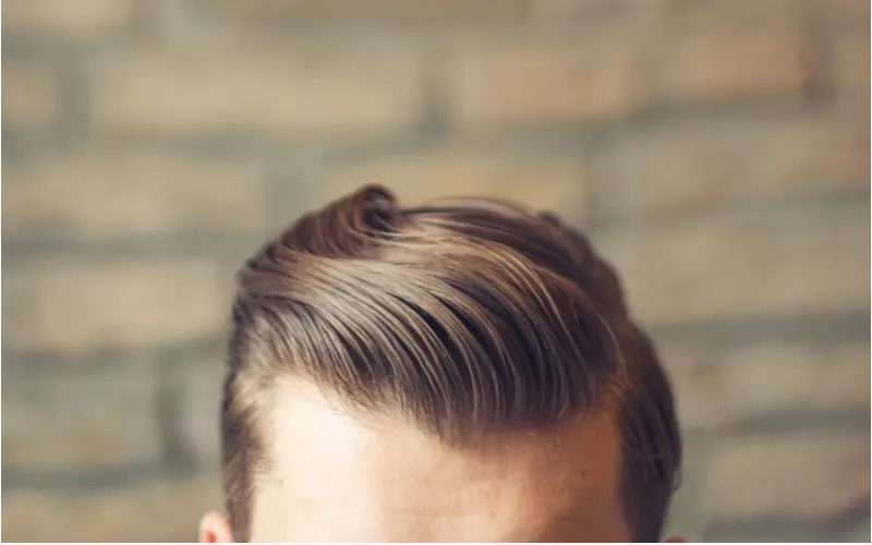 Caucasian male with hipster haircut on a guy with slicked back hair standing in front of a brick wall