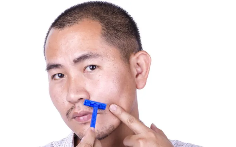 Thin Hair Buzzcut on an Asian man holding a blue razor to his face