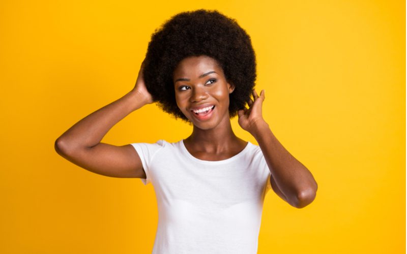 Đối với một phần về cách tạo một afro, một người phụ nữ đứng và ôm sau đầu khi mặc áo sơ mi trắng