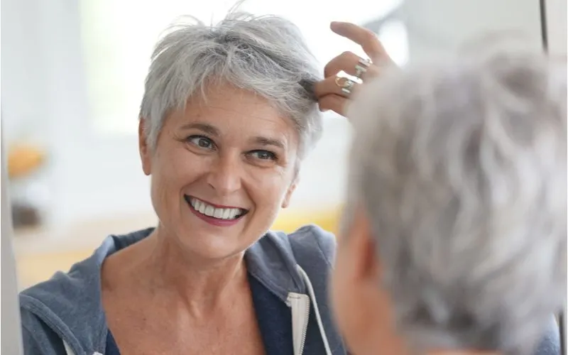 Image for a piece on what causes grey hair featuring a woman holding her bangs and looking at herself in the mirror