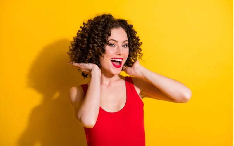 Woman with a curly bob haircut holds the end of her hair while wearing a red dress