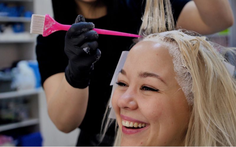 Image to help answer how often can you bleach your hair with an Asian woman sitting in a salon chair having her hair dyed with a bleach brush with a rattail end