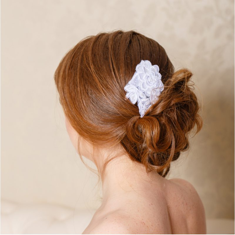 Young woman with an exposed back wears a classic floral bun while getting ready for a wedding