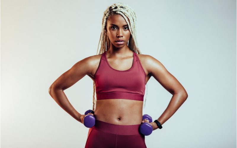 Athletic black woman wearing an edgy hairstyle, bleached box braids while she stands in a sports bra and yoga pants with her hands on her hips