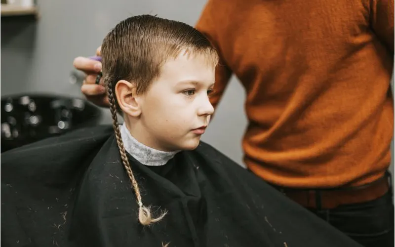 Boy with braids for men sitting in a barber's chair next to a guy in an orange sweater