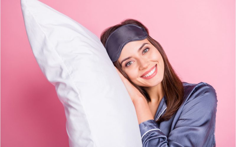 Woman in a pink room tilting her head and holding a pillow up to her face for a piece on how to keep hair straight overnight