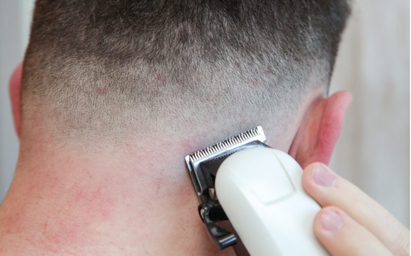 To help answer the question what is a bald fade, a guy with close-cut electric clippers trims the neckline of a pale man
