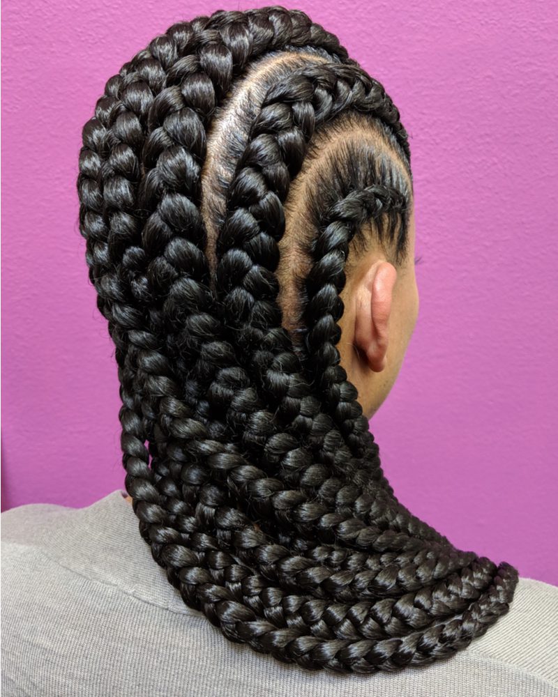 Black woman wearing a jumbo braid hairstyle standing in front of a purple wall