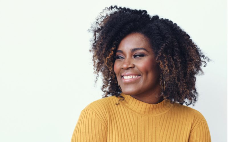 Image for a post on how to plop hair showing a naturally curly woman with a striped yellow sweater smiling and looking right