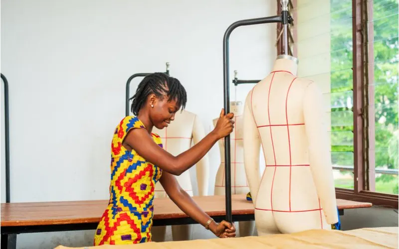 Black woman with tribal braids that are like mini dreads pulled to the side pushes a mannequin