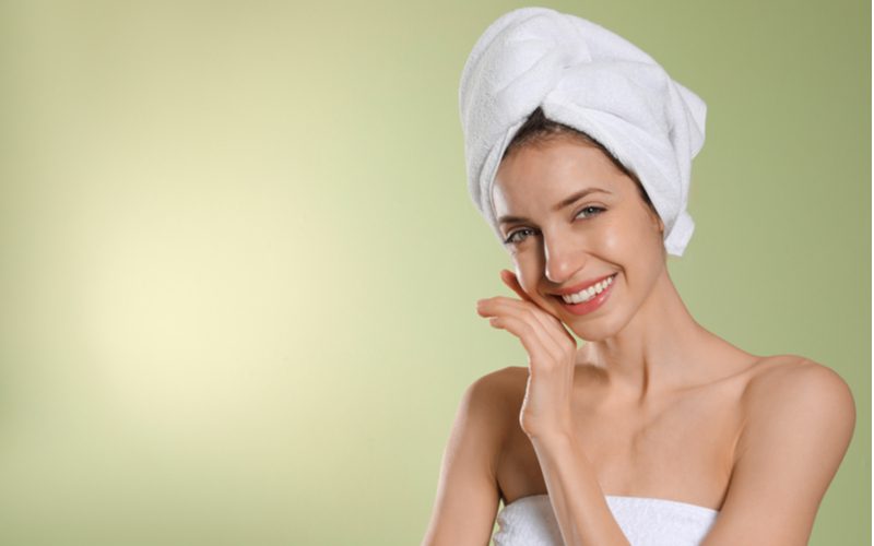 Gal plopping hair with a white linen towel and smiling while holding her hand to her cheek