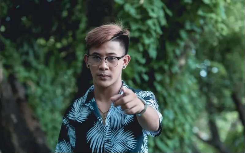 Asian man with gauged ears and glasses wearing a tropical shirt and a Two Block Burst Fade points at the camera