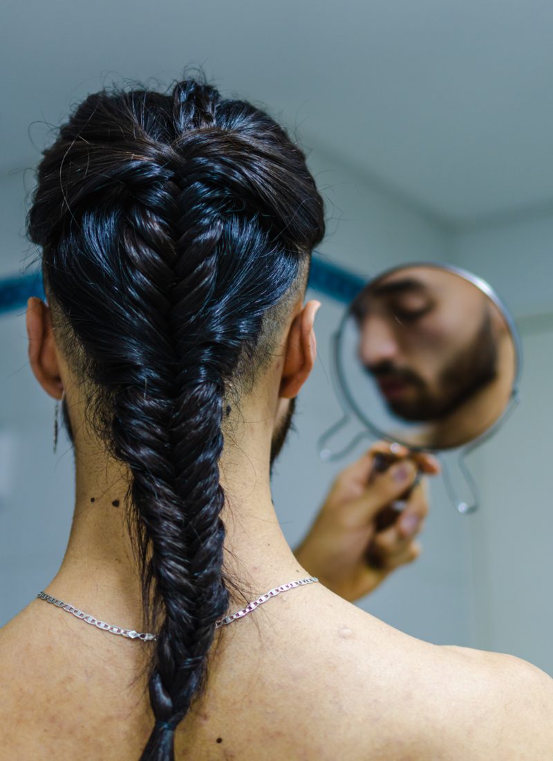 Young man with a fishtail braid for men looking at his scruffy beard in the mirror