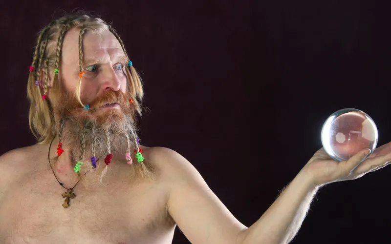 Guy with colorful braids for men on his beard and hair holding a glass sphere