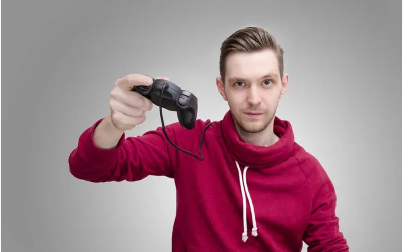 Guy with slicked back hair in a red hoodie holding a gaming controller up
