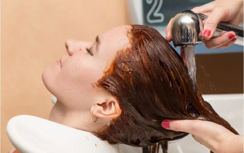 Image for a piece on how to get red out of hair featuring a woman with red hair getting it washed in a salon sink
