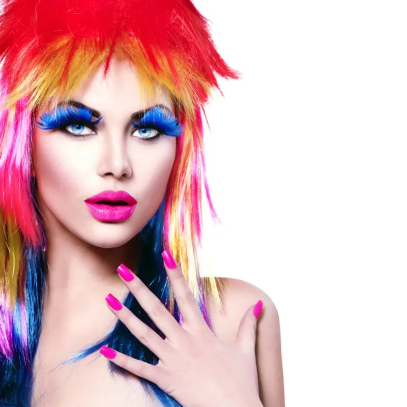Woman with purple nails and multicolored feathered hair stands in a white room and looks at the camera with an intense gaze