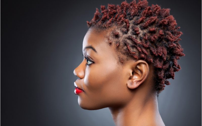Side profile of a black woman wearing a popular hairstyle, starter locs, that have been colored red at the ends