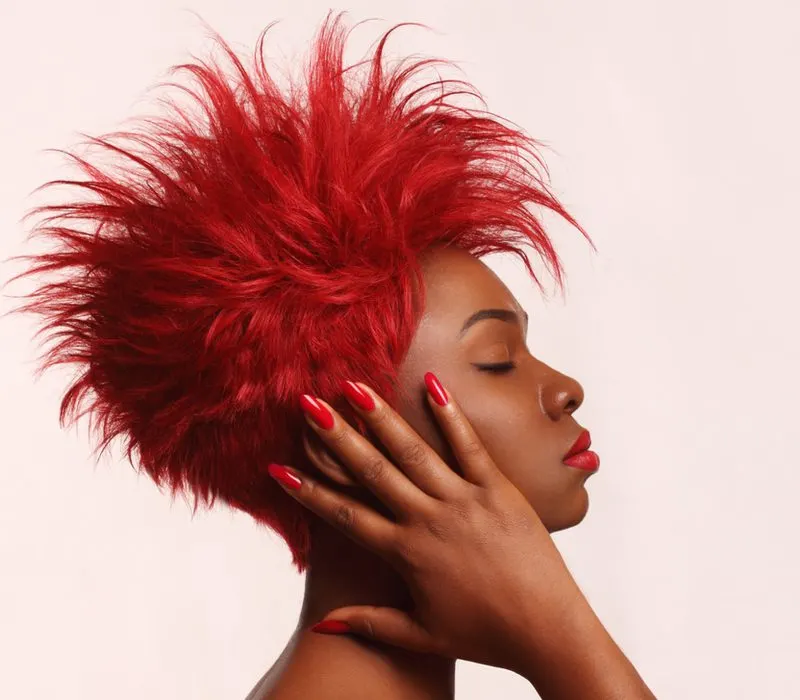 Punk black woman with red feathered hair spiked straight up holds the right size of her head
