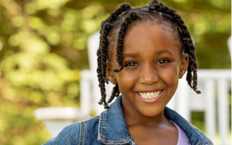 Kid-Friendly Box Braids on a girl with beads in her hair standing in front of a white fence