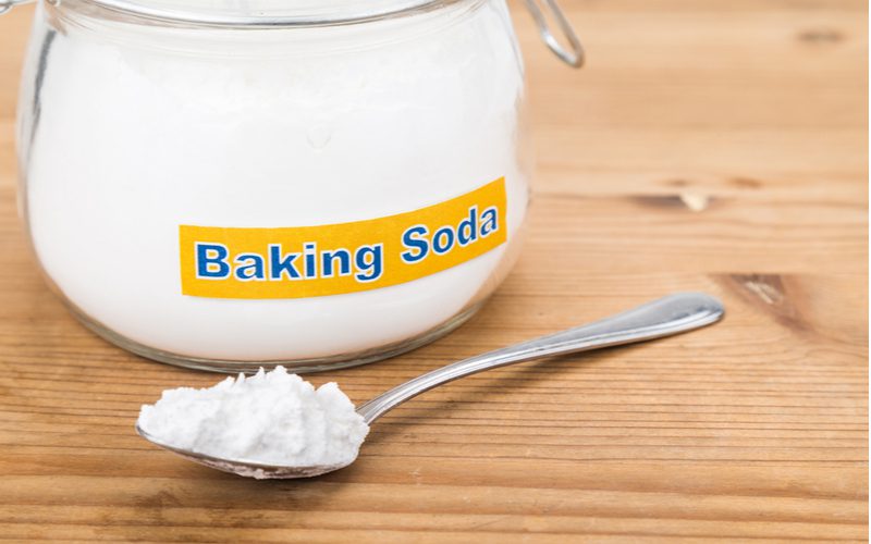 Spoonful of baking soda next to a glass jar sitting on a wooden table